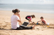 Woman attending phone call as kids go busy on the beach
