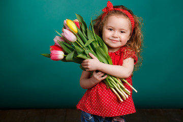 Spring portrait of a smiling little girl with red curly hair holding a bouquet of multi-colored tulips as a gift, isolated on a light green background in the Studio.A cute little girl with a bouquet o