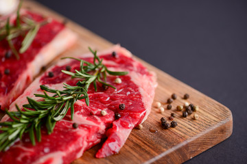 Fresh raw steak on wooden cutting board over black background with spices, top view.