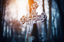 An Old Rusty Beautiful Crooked Cross Stands In The Middle Of A Gloomy Forest Illuminated By The Rays Of The Setting Sun.