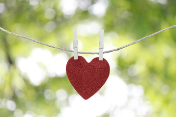 Wall Mural - Red heart hanging on a hemp rope on the green bokeh background.