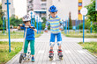 © pahis - Two kid boy on roller skates and his sibling brother on scooter wrapped in park. Children wearing protection pads for safe roller skating ride. Active outdoor sport for kids