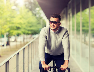 Wall Mural - lifestyle, transport and people concept - happy smiling young man in sunglasses riding bicycle on city street