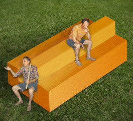 The two men are sitting on the impossible timber in the meadow. One holds a wooden ruler, the second thinks of something.