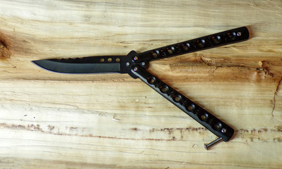 Butterfly knife on a wooden background. Black knife butterfly balisong close-up. Cold steel. A razor-sharp knife.