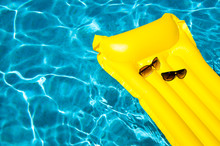 His And Hers Sunglasses Resting On Empty Yellow Inflatable Raft Floating In Bright Blue Swimming Pool