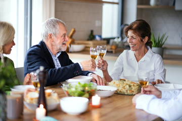 Wall Mural - Group of senior friends at dinner party at home, clinking glasses.