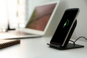 Mobile phone with wireless charger on white table. Modern workplace accessory