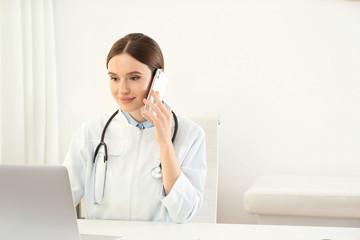 Wall Mural - Young female doctor talking on phone at table in office