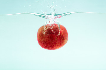 Aufkleber - Perfect pomegranate flying into clear water on blue background