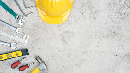 Flat lay craftsman tool concept on old concrete cement wall background with safety helmet and standard tools,  spanner, wrench,Hammer, screwdriver and measurement Tool, Top view with copy space