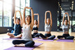 © Kawee - Group of Multi ethics people learning Yoga class in fitness club. Female Asian instructor leading Meditate sitting stretch hand and arms pose, students follow behind. Yoga for health, wellness concept