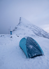 Wall Mural - man climber with tent camping on snow mountain peak in gloomy