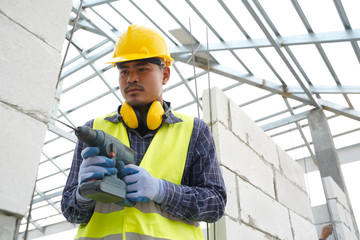 Poster - Workers use a drill bit,Engineer wearing safety equipment (helmet and jacket) uses a power drill to mount a plaster wall panel.