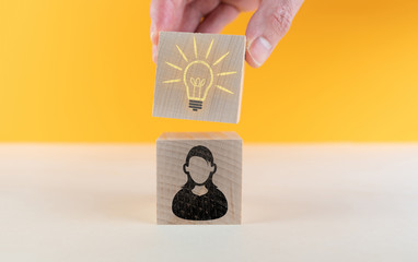 Wall Mural - person having an idea concept, female avatar icon and glowing light bulb on wooden cubes against orange background