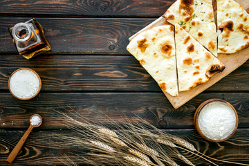 Focaccia ingredients. Wheat ears, flour, oil near bread on dark wooden background top-down copy space