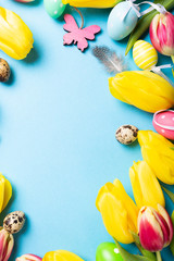 Wall Mural - Happy Easter card. Frame with yellow tulips and easter quail eggs with copy space for text on blue background. Top view.