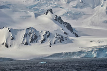 View Of Rocky Hillside Peak Jutting Out Of Antarctic Snowy Glaciers With Mountain Background