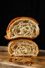 Canvas Print - A croissant cut in half, one half on top of the other, on a wooden board on black background