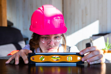 young caucasian woman architect wearing a pink hard hat and protective eyewear, she measuring horizontal surface with a spirit bubble level tool