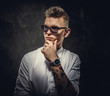 Cool and tattooed hipster male model posing in a studio wearing a white shirt, sunglasses, standing in front of the grey background, looking assertive and interested, close up portrait
