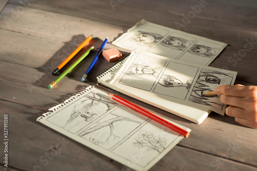 Artist drawing an anime comic book in a studio. Wooden desk, natural light