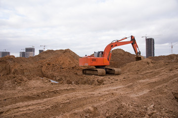 Wall Mural - Red Excavator at building under construction. Backhoe digs the ground for the foundation and for laying sewer pipes. Renovation program. Buildings industry background