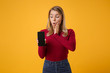 © ViDi Studio - Amazed young blonde woman girl in casual clothes posing isolated on yellow orange background. People lifestyle concept. Mock up copy space. Hold mobile phone with blank empty screen put hand on cheek.