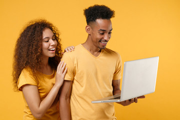 Wall Mural - Funny young friends couple african american guy girl in casual clothes isolated on yellow orange wall background. People emotions lifestyle concept. Mock up copy space. Working on laptop pc computer.