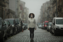 Asian Woman In Antiviral Mask Stands In The Middle Of A Deserted Street In Foggy.