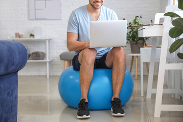 Poster - Man with laptop sitting on fitness ball at home