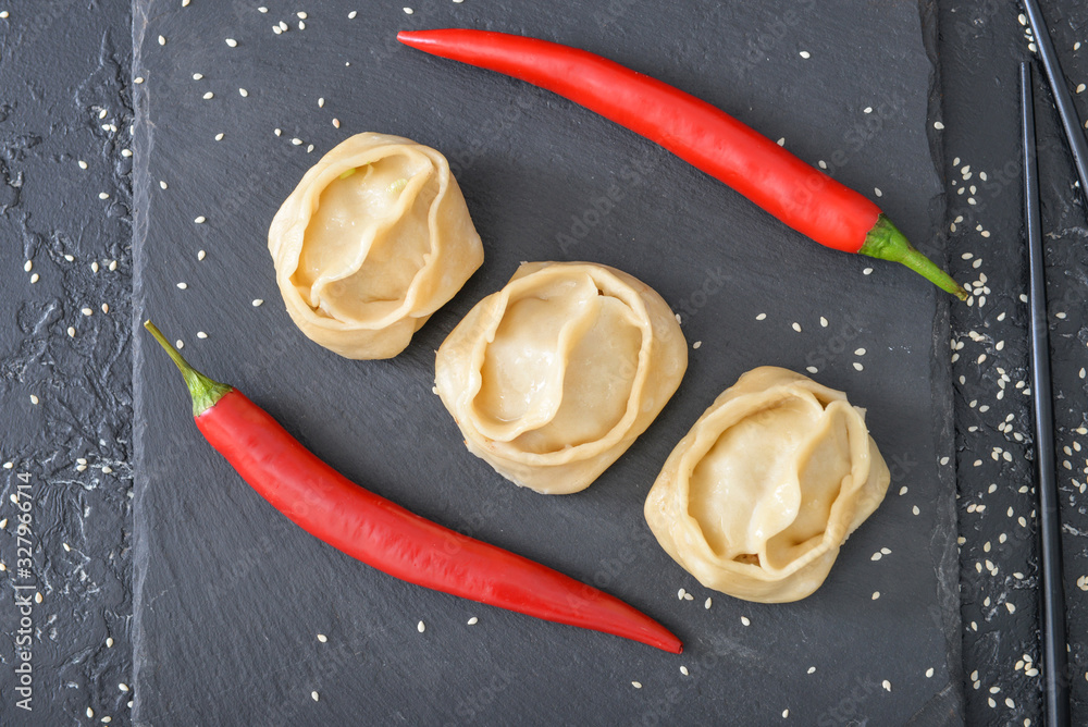 Slate plate with oriental dumplings and chili pepper on dark background