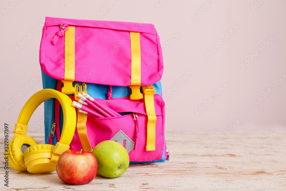 School backpack, headphones and apples on table against color background