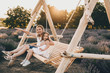 © Strelciuc - Lovely caucasian mother and her small daughter sitting in a swing with a lavender field on background