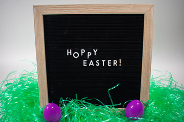 A Black Happy Easter Sign With White Letters, Easter Grass, and Easter Eggs