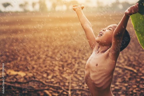 Fotografía Climate change, Asian boy enjoy with first falling rain season on dry cracked land
