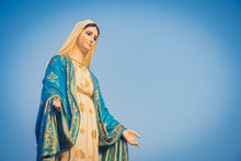 Close-up Of The Blessed Virgin Mary Statue Figure. Catholic Praying For Our Lady - The Virgin Mary. Blue Sky Copy Space On Background.
