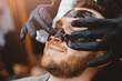 © Parilov - Barber applies black charcoal mask to man face to clean pore skin and remove acne from nose, spa salon