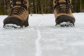 Hiking boots on both sides of a crack in the ice with out of focus forest in the background. Decision, right and wrong, left or right.