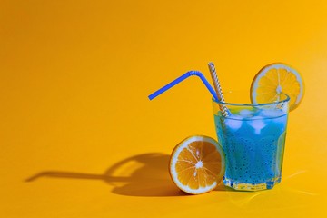 Wall Mural - Amazing blue cocktail with ice, orange, chia seeds in glass on gradient orange background. Summer vacation and holiday concept. Healthy nutrition and natural ingredients. Copy space.