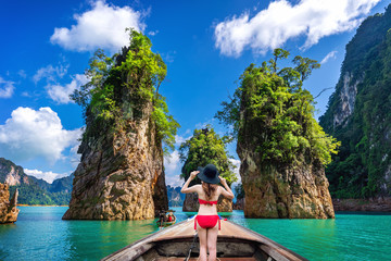 Wall Mural - Beautiful girl standing on the boat and looking to mountains in Ratchaprapha Dam at Khao Sok National Park, Surat Thani Province, Thailand.