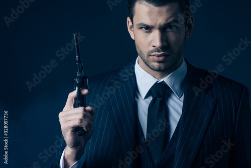 Photographie Front view of gangster holding gun and looking at camera on dark blue background
