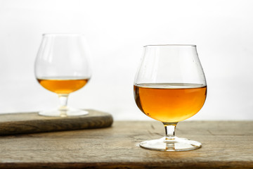 Cognac \ whiskey in cognac glass on wooden table, golden color spirits splashing on white background