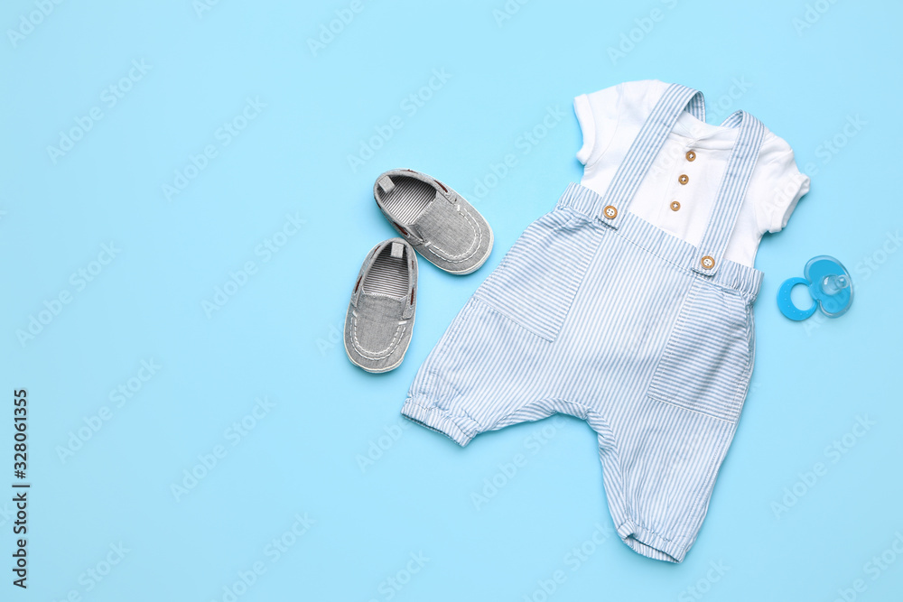 Baby clothes with booties and pacifier on color background