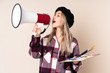 Teenager artist girl holding a palette isolated on blue background shouting through a megaphone