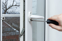 The Handyman Opened And Adjusts The Plastic Window In The House. Adjustment Of The Lock Mechanism With A Screwdriver. Installation, Configuration And Maintenance Of Plastic Windows Made Of PVC.