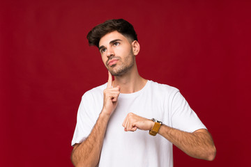 Young man over isolated background with wrist watch and thinking an idea