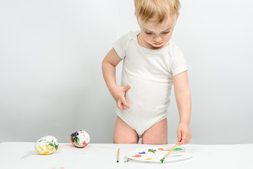 Children paint eggs for Easter on a paper sheet. Child 2 years. Preparation for Easter. Multi-colored paint, hands in the frame paint the eggs. handmade chickens.