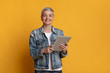 © Prostock-studio - Smiling mature woman with digital tablet in hands on yellow background