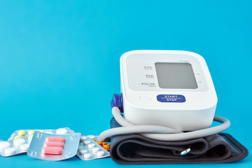 Digital blood pressure monitor and medical pills on a blue background. Healthcare and medicine concept